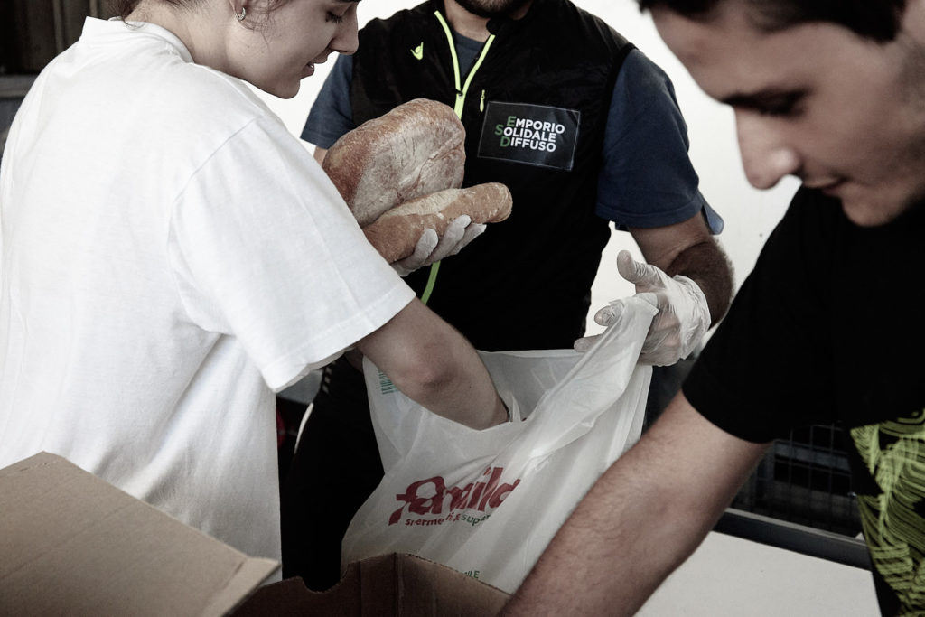 Volontari di Emporio Solidale Diffuso riempiono di pane dei sacchetti della spesa.